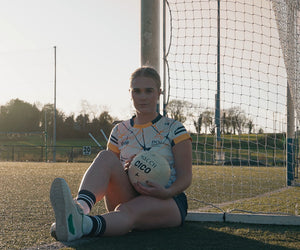 Person sitting on a soccer field holding a ball with a goalpost in the background